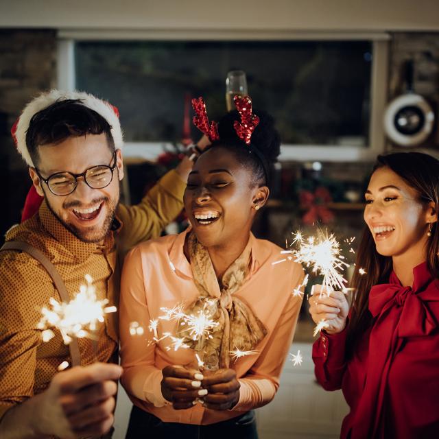 Group of cheerful friends using sparklers and celebrating on New Year's eve at home.